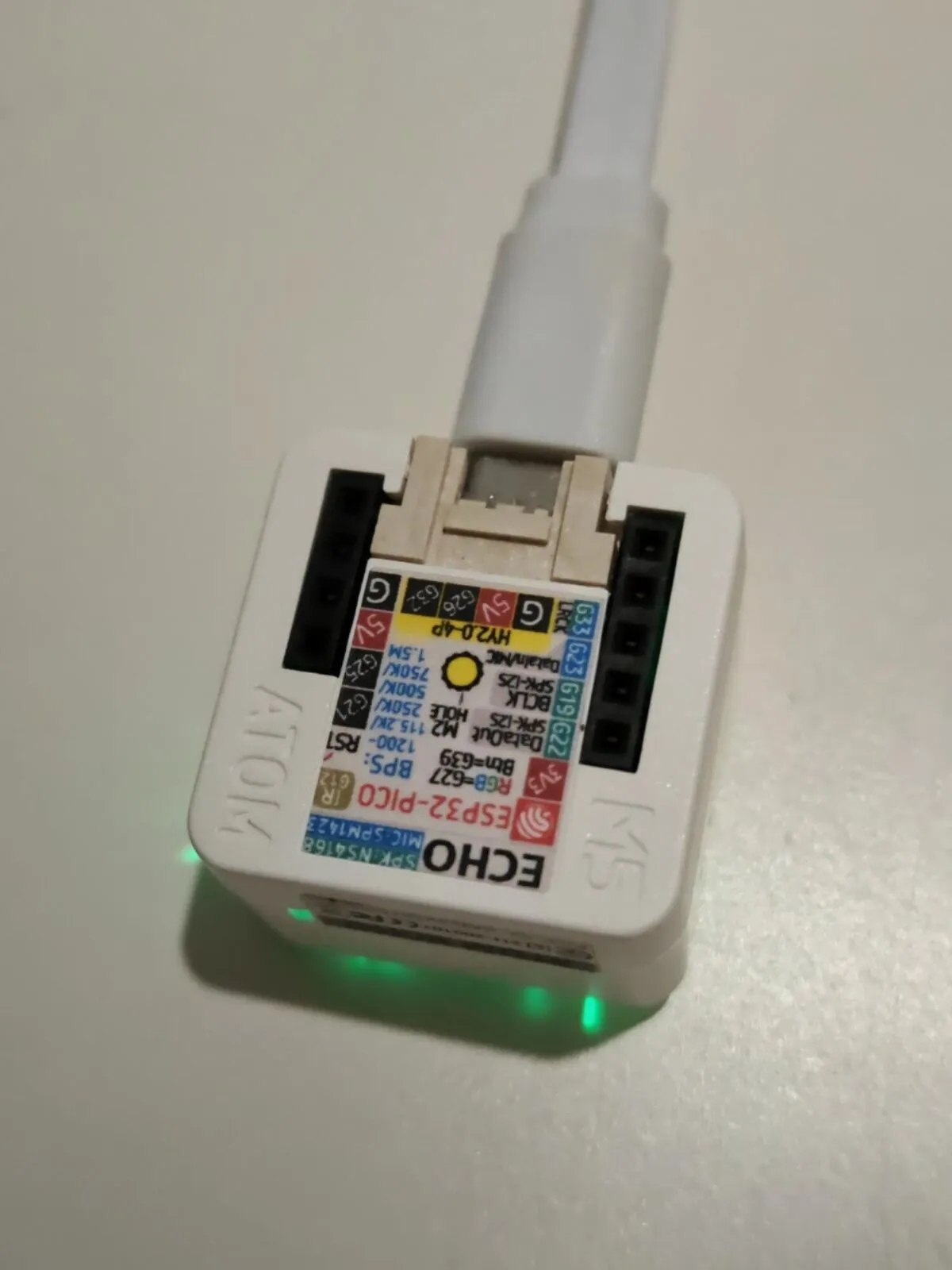 The bottom of the Atom Echo: a printed label with its pinout, ESP32-PICO, the microphone and speaker chips, and the USB-C cable plugged in