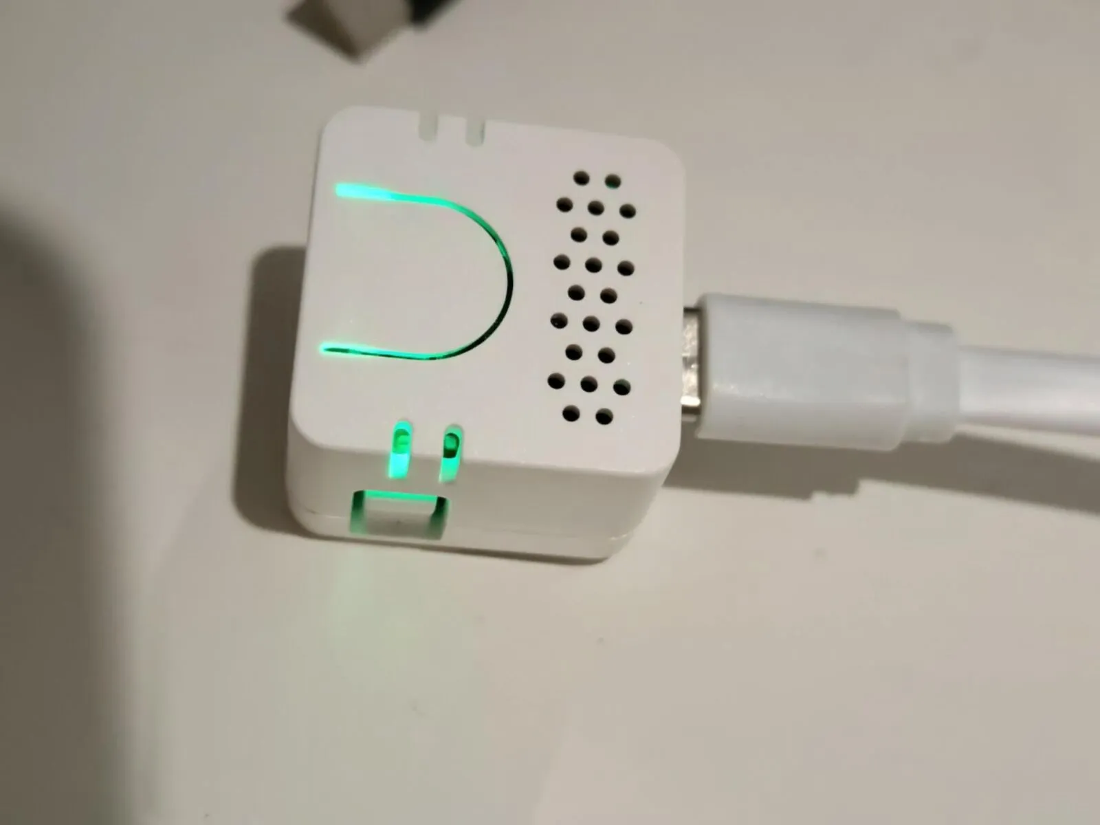 The Atom Echo from the side, its U-shaped light and two small slots glowing green, with the speaker grille next to them