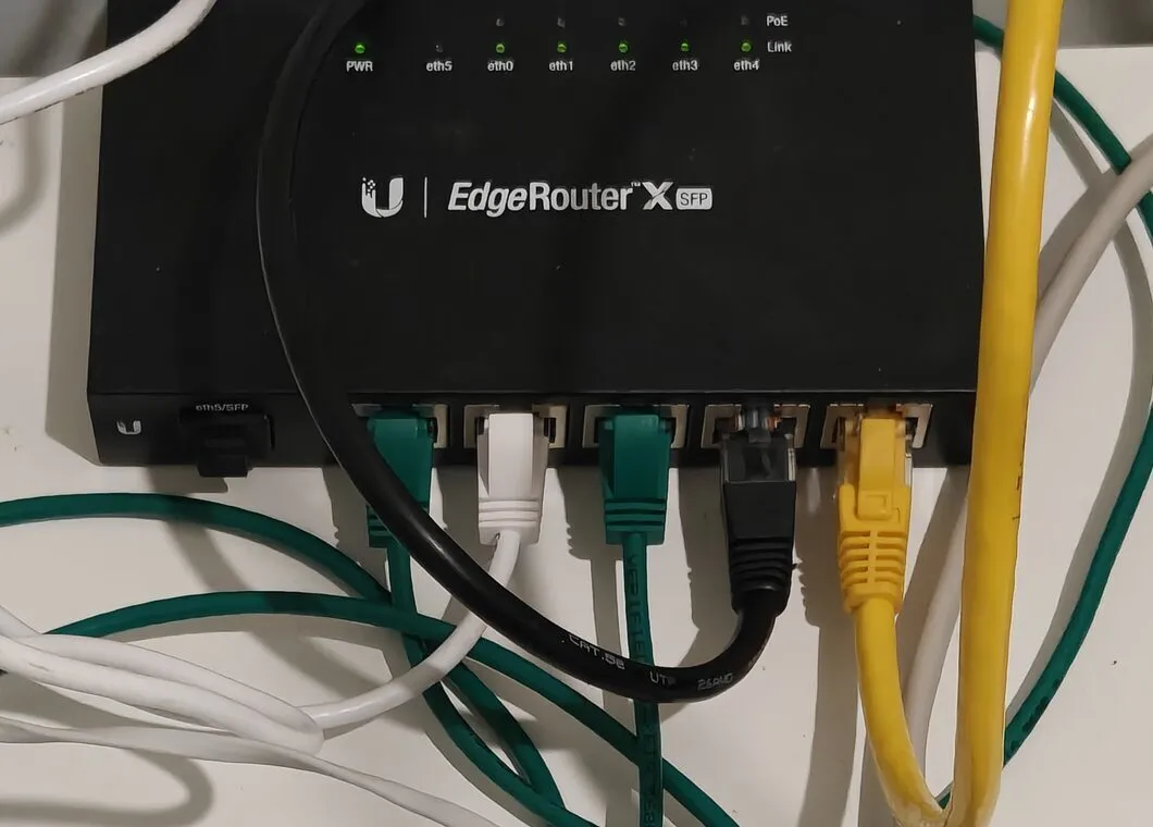A black EdgeRouter X SFP from above, five Ethernet cables plugged into its ports and the green link lights on