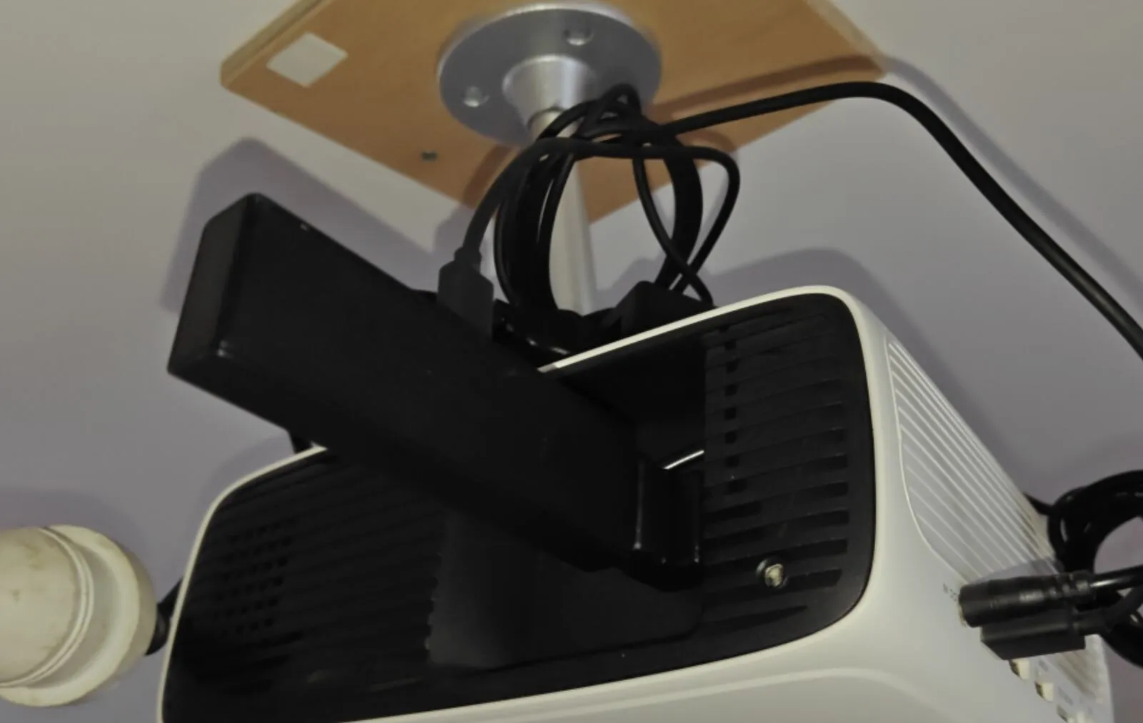 A black Fire TV Stick plugged into the HDMI port on top of a white projector mounted on the ceiling