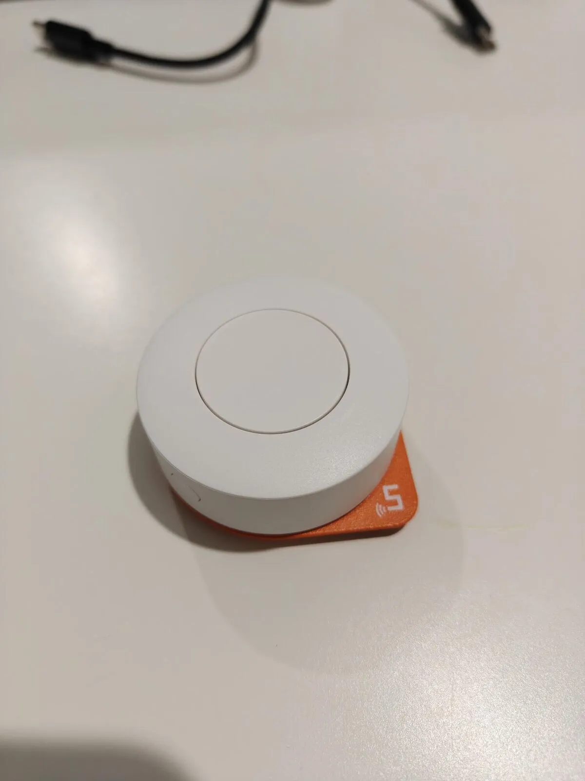 A round white Sonoff button on an orange stick-on base