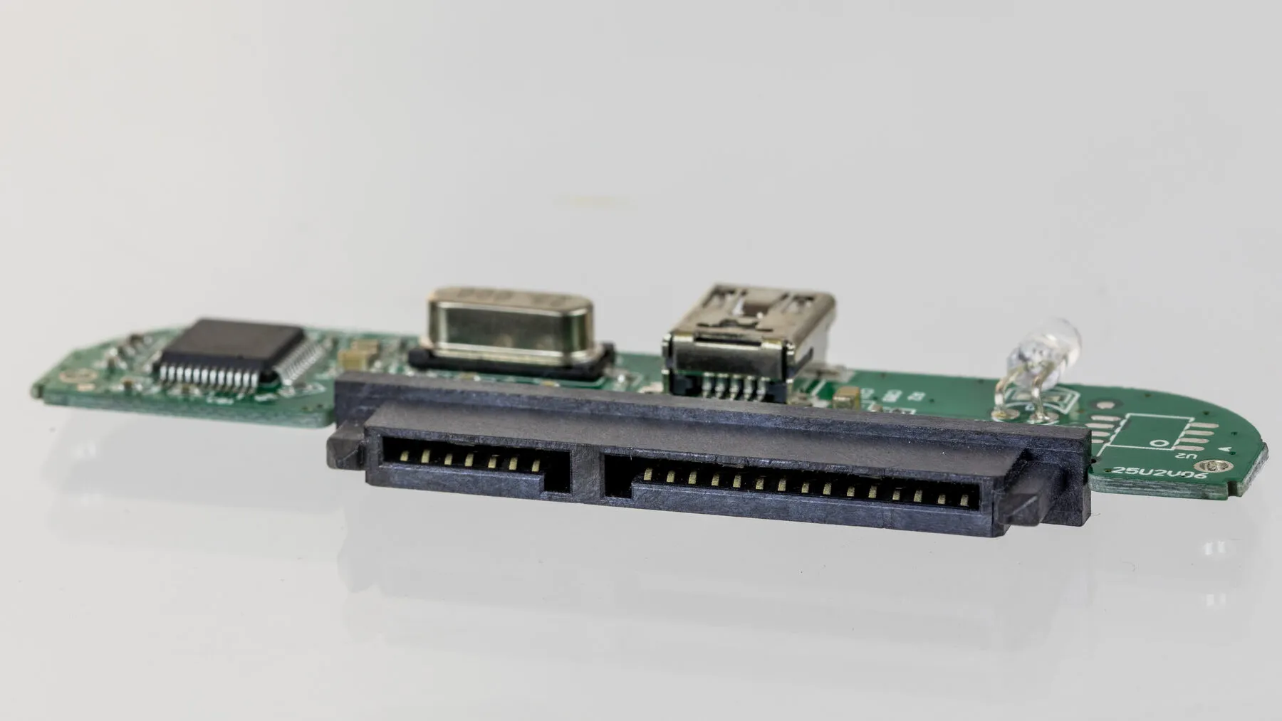 A small green circuit board: a square chip on the left, a crystal, a mini-USB socket and a black SATA connector along the front