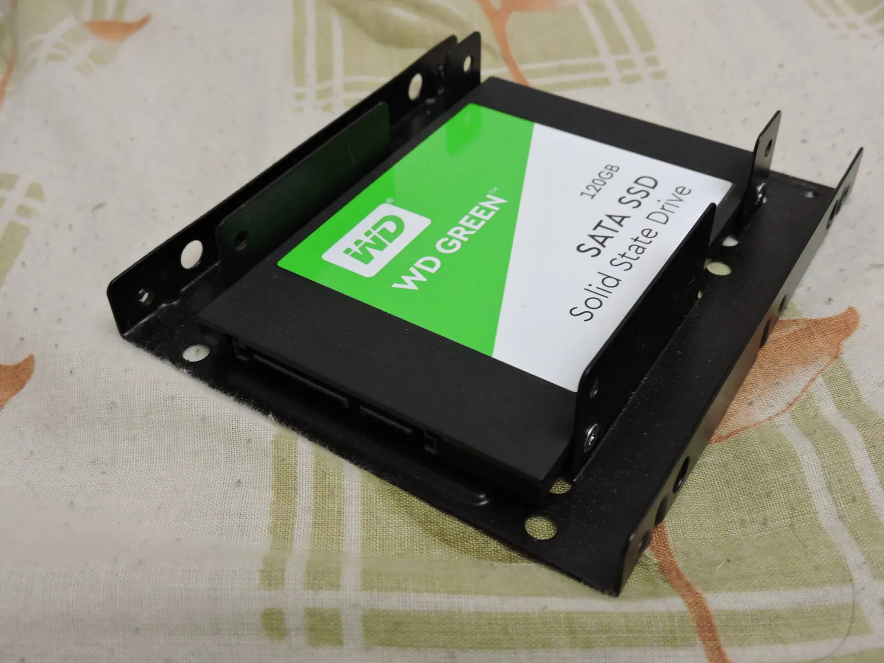A WD Green 120 GB SATA SSD, black with a green and white label, sitting in a metal drive bracket