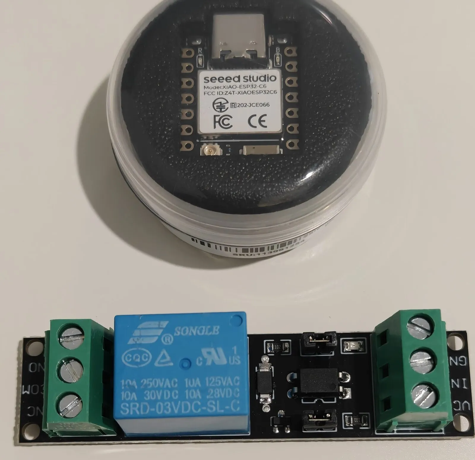 A Seeed XIAO ESP32-C6 in its plastic tub, and a 1-channel relay module with a blue Songle relay and screw terminals
